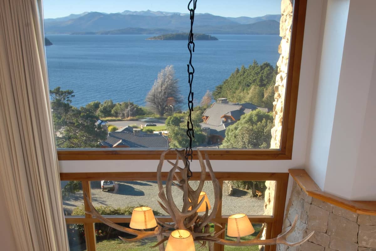 Una sala de estar acogedora con un gran ventanal con vistas a un lago, una chimenea y una araña.