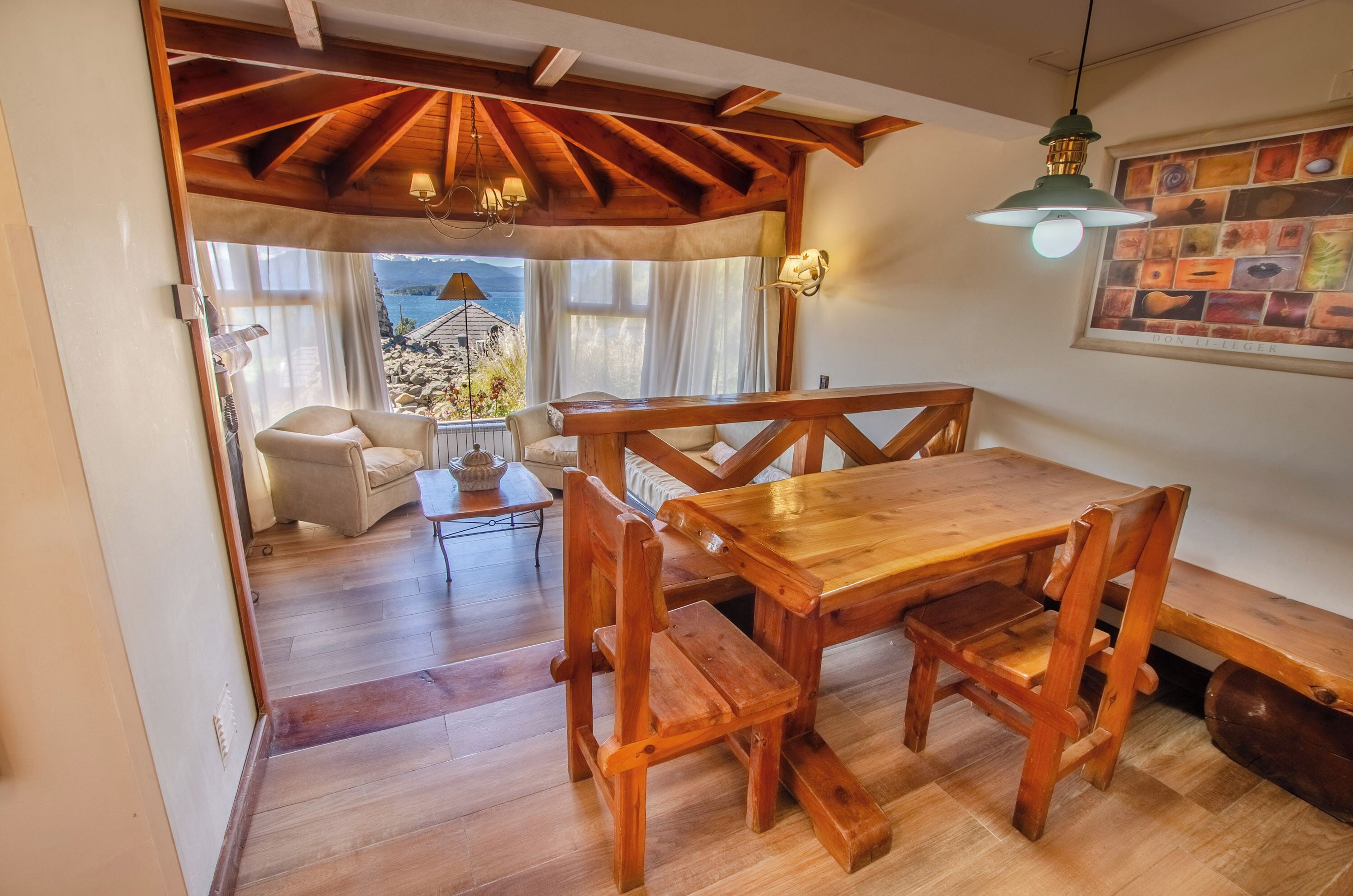 A wooden dining table with chairs, a chandelier, and a view of a house and mountains.