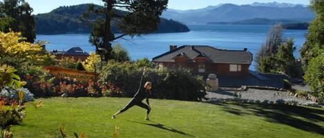 A person practicing yoga on a grassy area with a lake and mountains in the background.