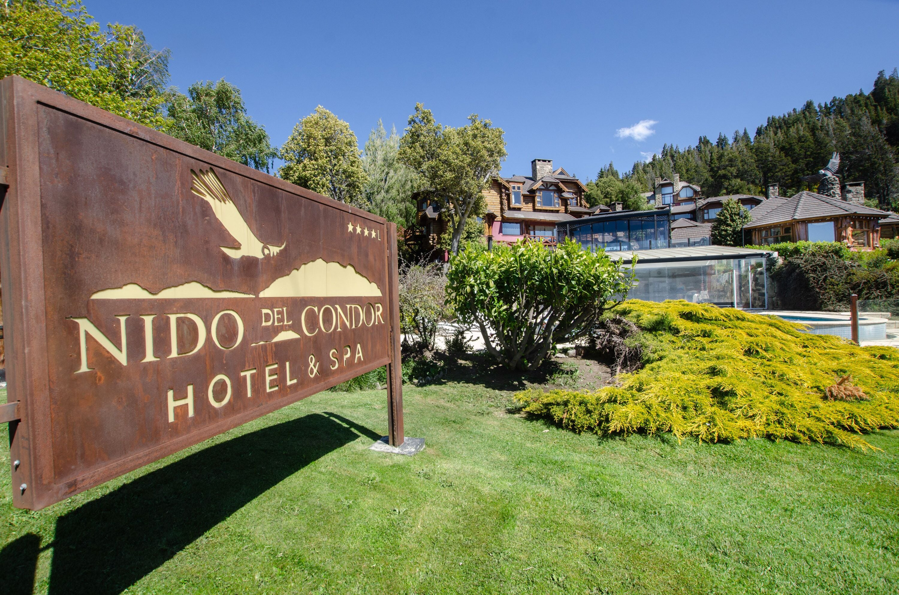 Une enseigne pour l’hôtel et le spa Nido del Condor, avec un motif représentant une montagne et un aigle, le tout entouré de verdure et de bâtiments modernes.