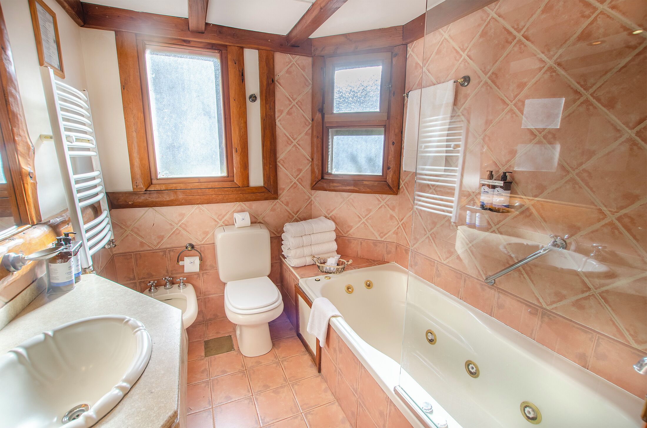 Un baño con bañera, inodoro, lavabo y una ventana con marcos de madera.