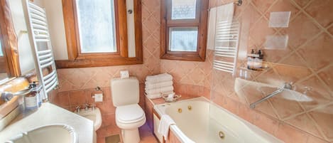 Un baño con bañera, inodoro, lavabo y una ventana con marcos de madera.