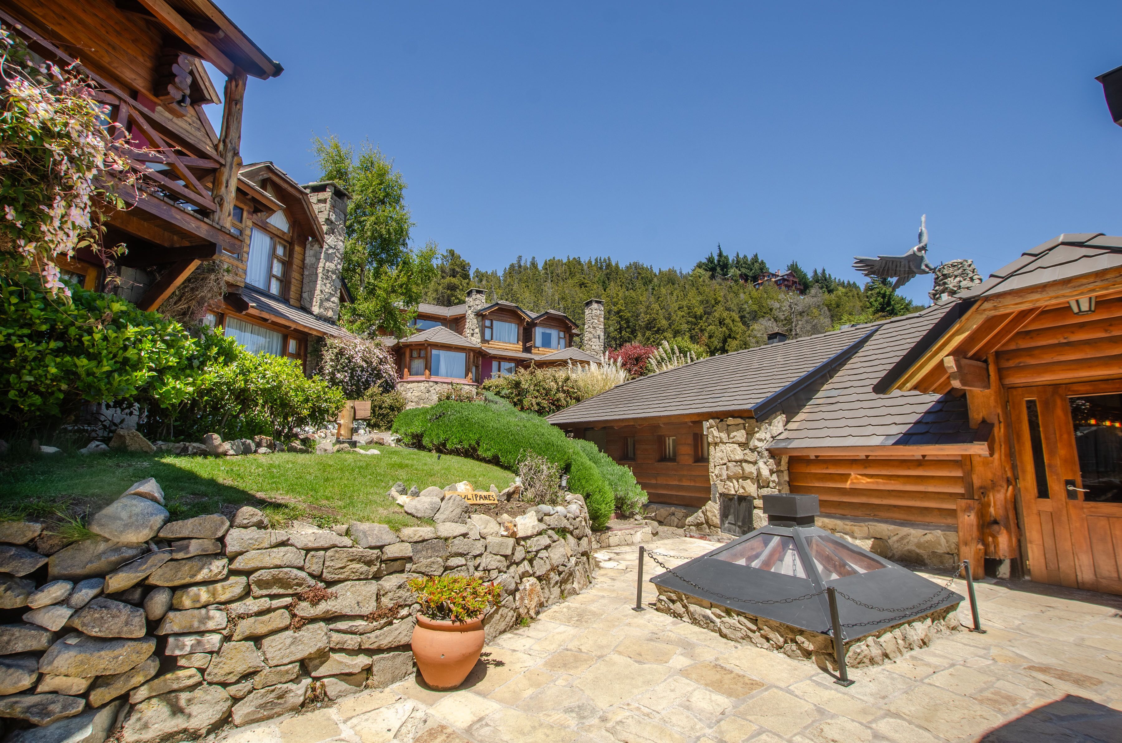 A log cabin with stone walls, a stone fireplace, and a patio area with a barbecue grill.