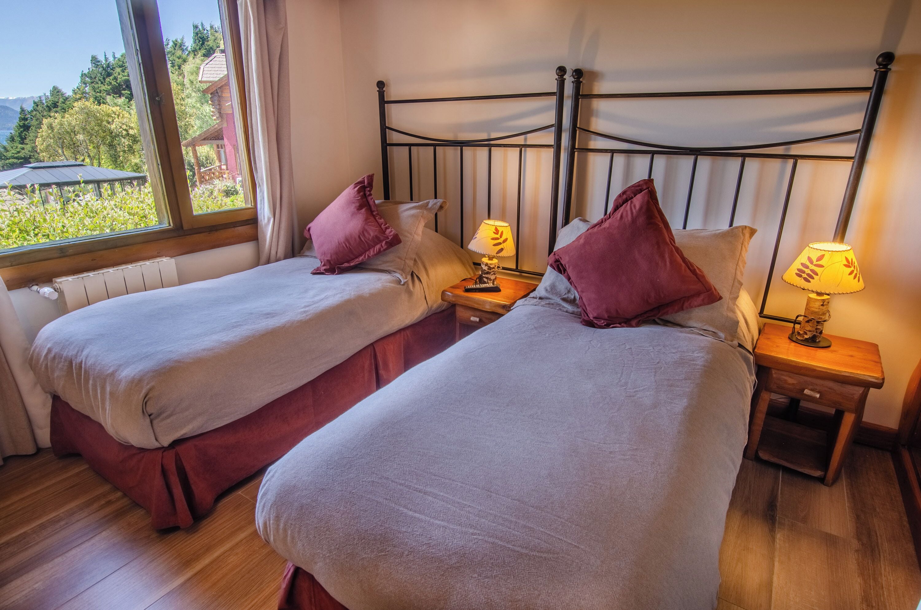 Habitación con dos camas, cada una con una mesita de noche de madera, una lámpara y vistas al exterior.