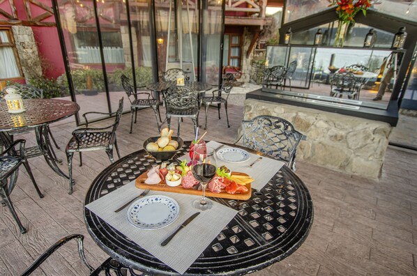 An outdoor dining area with round tables and chairs, a buffet with various foods, and a stone wall in the background.