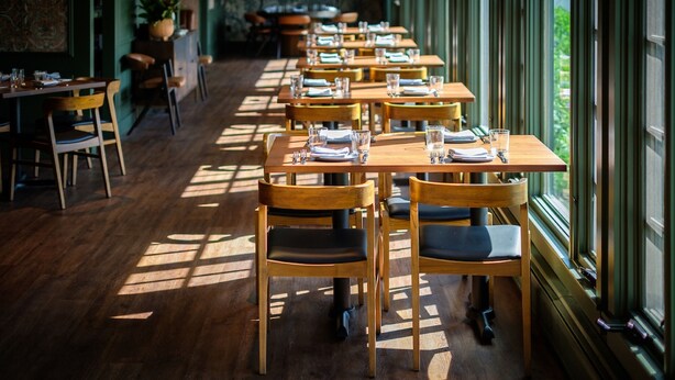 A restaurant with wooden tables and chairs, arranged in a row, with large windows on one side. - The New London Inn (New London)