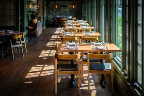 A restaurant with wooden tables and chairs, arranged in a row, with large windows on one side. - The New London Inn (New London)