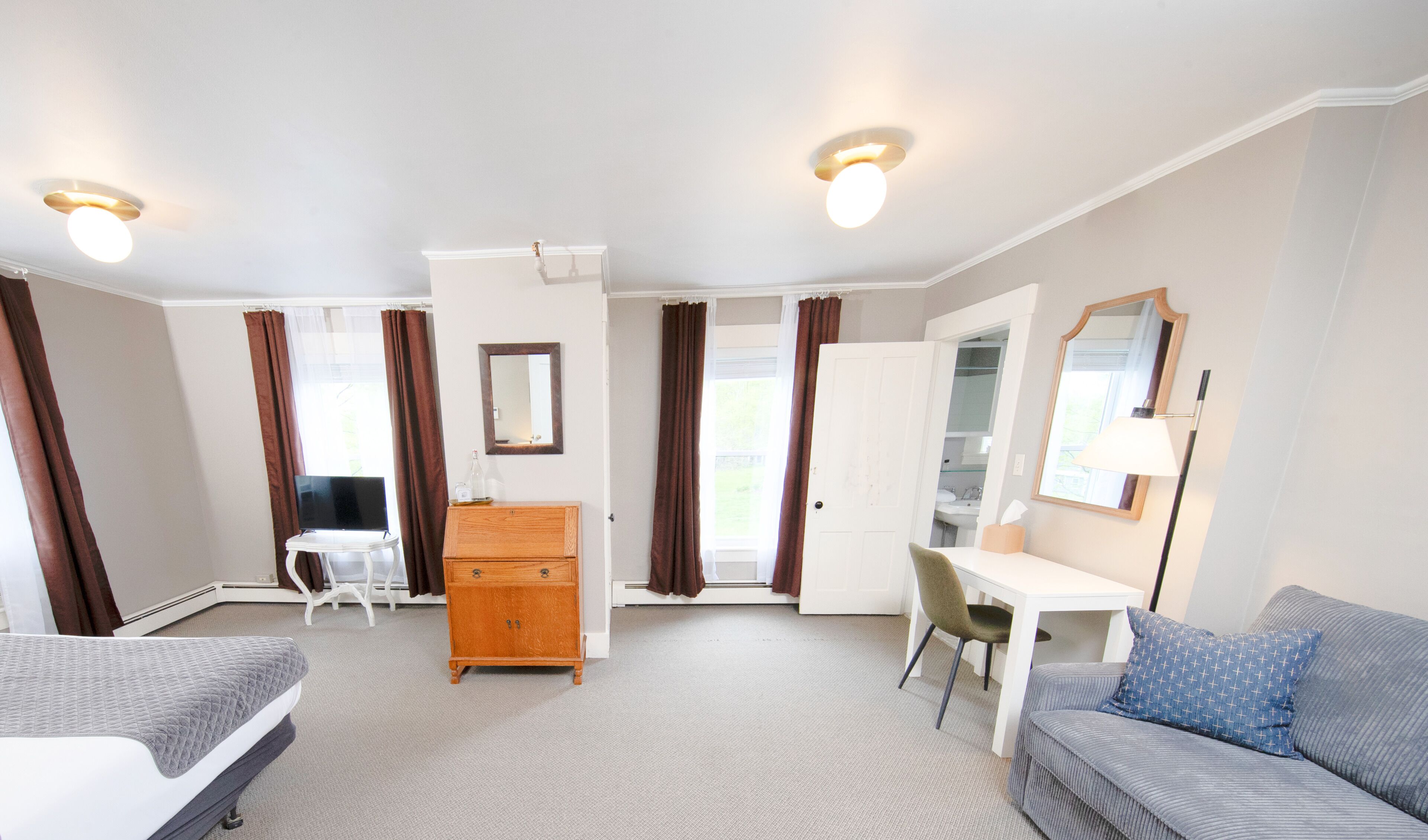 A room with a bed, a desk, a chair, a dresser, a mirror, and a window with curtains.