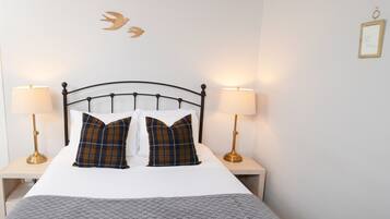 A neatly made bed with plaid pillows, two bedside lamps, and a wall-mounted bird decoration.
