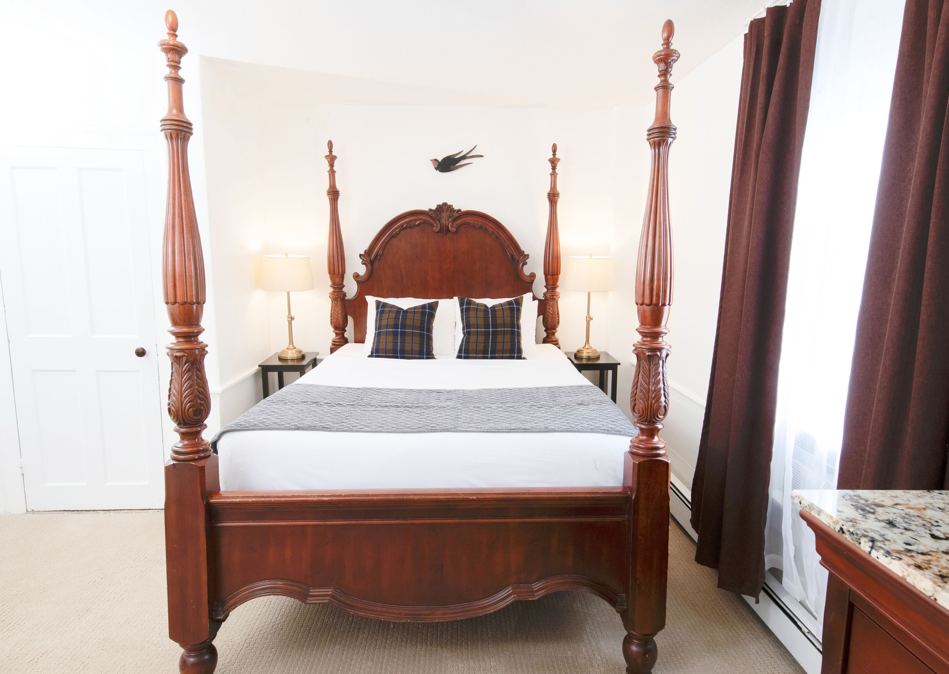 Una cama con dosel con cabecera de madera, dos mesitas de noche con lámparas y vistas al exterior a través de una ventana con cortinas.