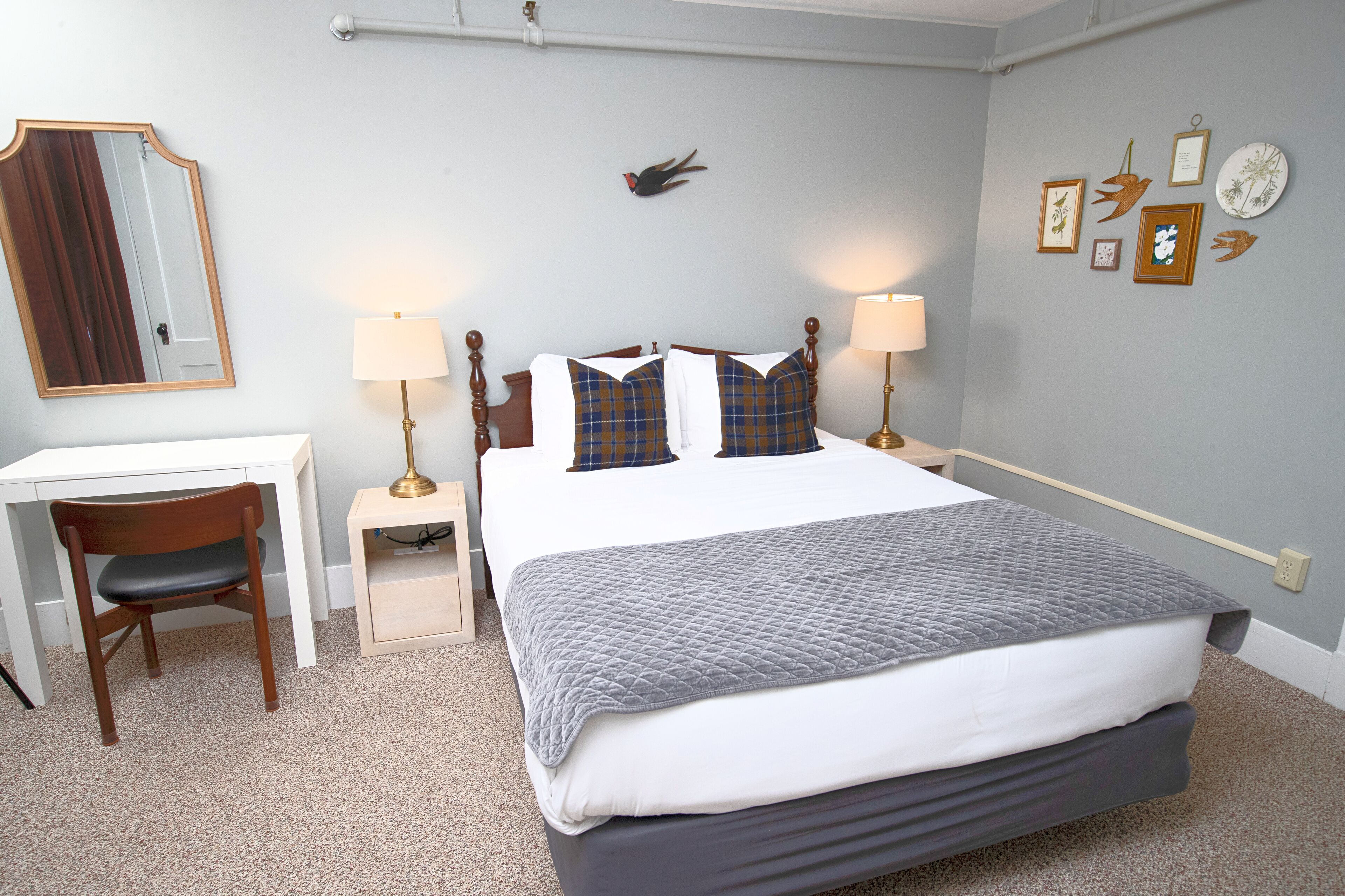 A neatly arranged hotel room with a bed, desk, chair, and bedside lamps.