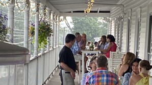 A covered outdoor seating area with tables and chairs, a person in an apron, and various beverages on the table. - The New London Inn (New London)