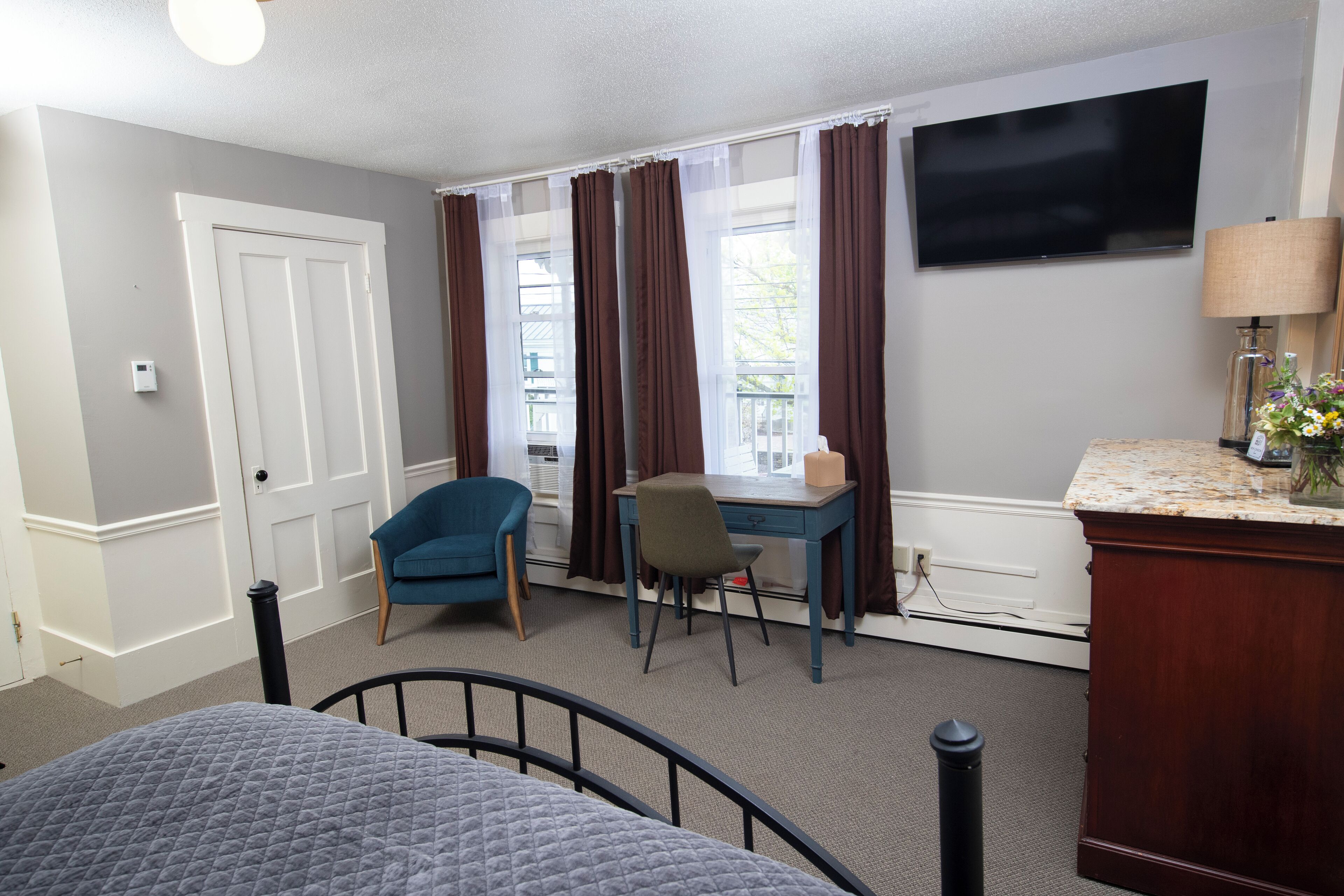A hotel room with a bed, a desk, a chair, a TV, and a window with curtains.
