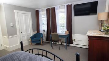 A hotel room with a bed, a desk, a chair, a TV, and a window with curtains.