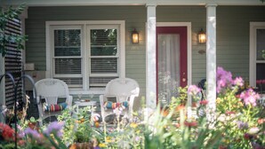 A porch with two wicker chairs, a small table, and a red door. - Hidden Garden Cottages & Suites (Saugatuck)