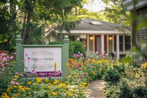 A sign for Hidden Garden cottages & suites with a garden path leading to a building.