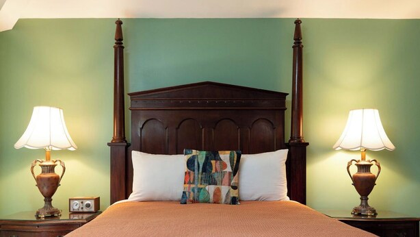 A four-poster bed with a wooden headboard, two bedside lamps, and a colorful throw pillow. - Hidden Garden Cottages & Suites (Saugatuck)