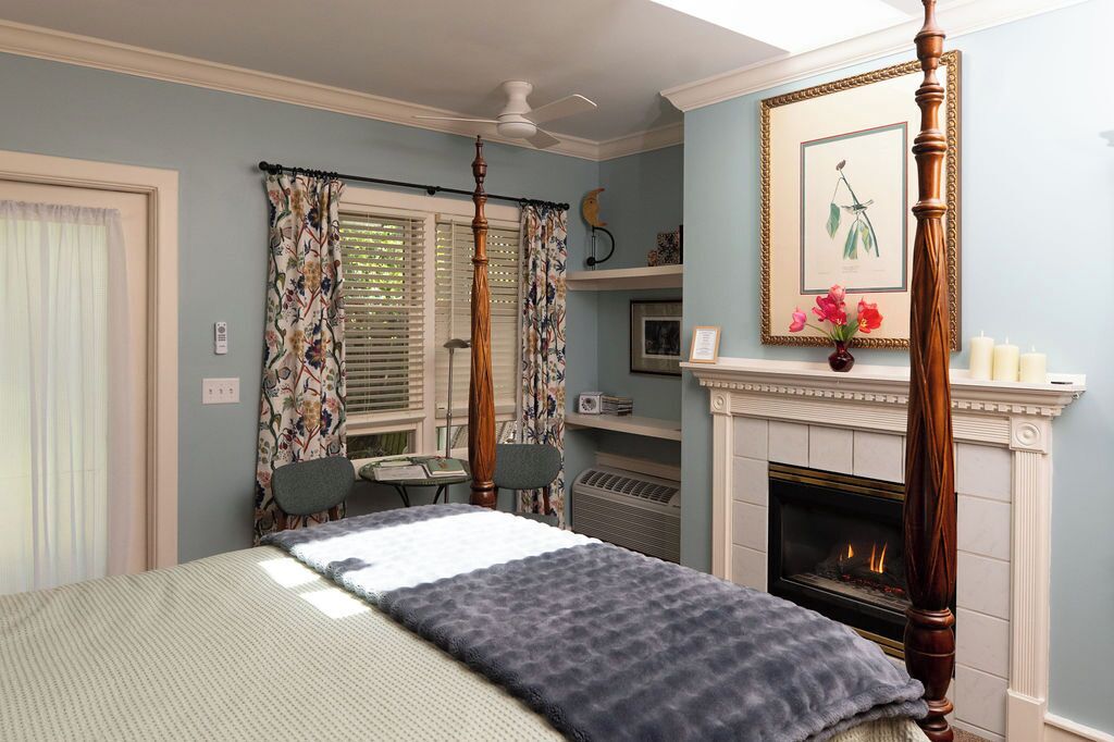Un dormitorio con cama con dosel, chimenea, ventilador de techo y escritorio con silla.