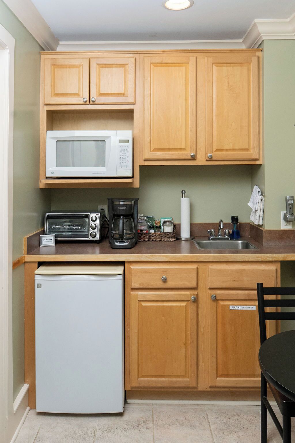 Eine kompakte Küche mit Holzausstattung, einer Mikrowelle, einem Toaster, einer Kaffeemaschine und einem Kühlschrank.