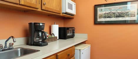 Eine Küche mit Holzausstattung, einer Mikrowelle, einer Kaffeemaschine, einem Kühlschrank und einem gerahmten Bild an der Wand.