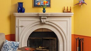 A room with a fireplace, a blue vase with flowers, a framed painting, and a decorative starfish on the wall. - Hidden Garden Cottages & Suites (Saugatuck)