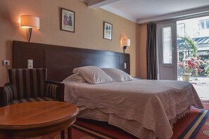 Una habitación de hotel con una cama, una silla, una mesa y dos lámparas fijadas a la pared.