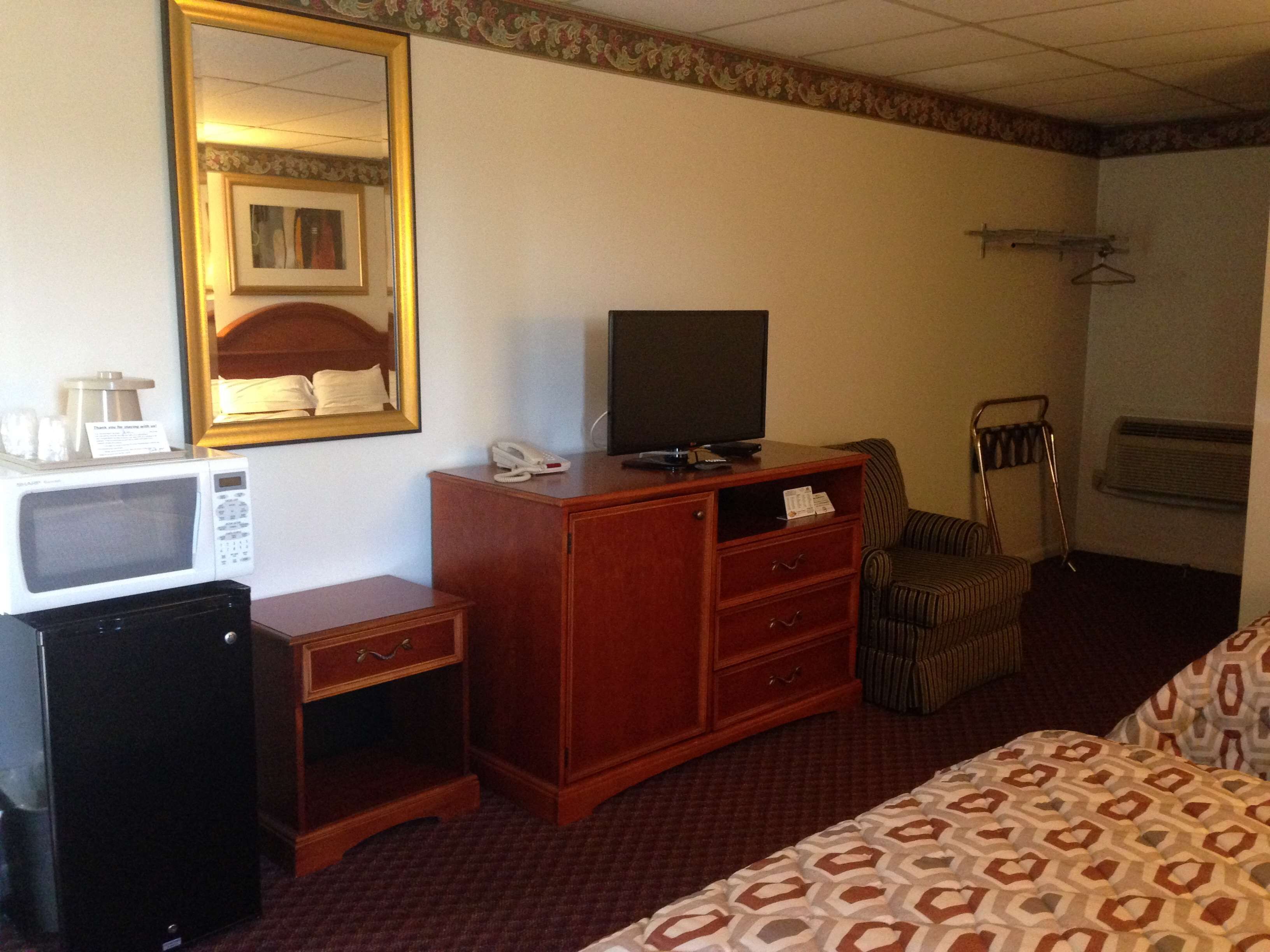 A hotel room with a bed, a wooden dresser, a microwave, a television, and a small refrigerator.