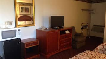 A hotel room with a bed, a wooden dresser, a microwave, a television, and a small refrigerator.