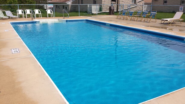 Una piscina rectangular con agua azul cristalina, rodeada de sillas de descanso y una terraza de concreto.