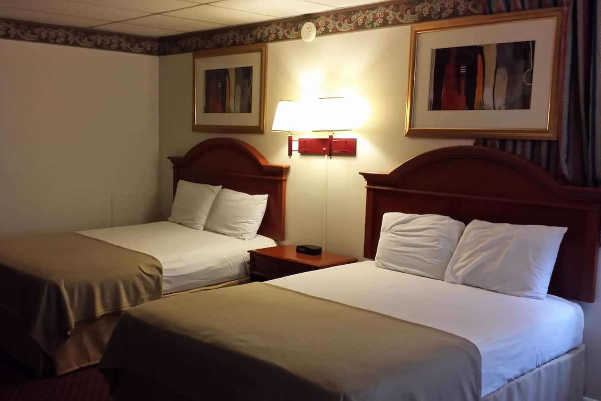 A hotel room with two single beds, a nightstand with a lamp, and a framed picture on the wall.