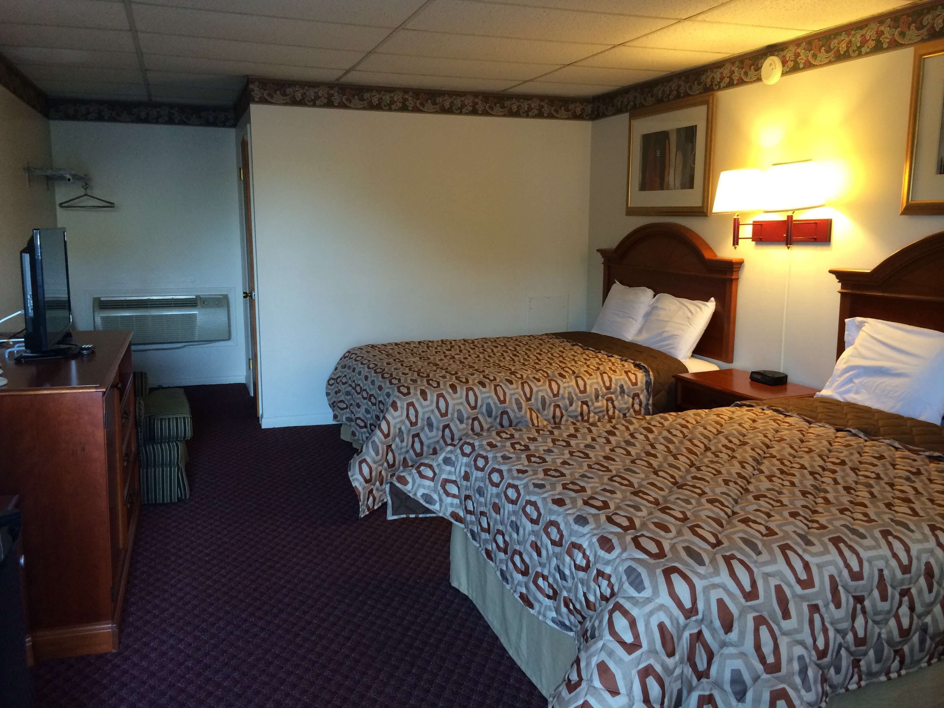 A hotel room with two beds, a desk, a television, and a lamp.