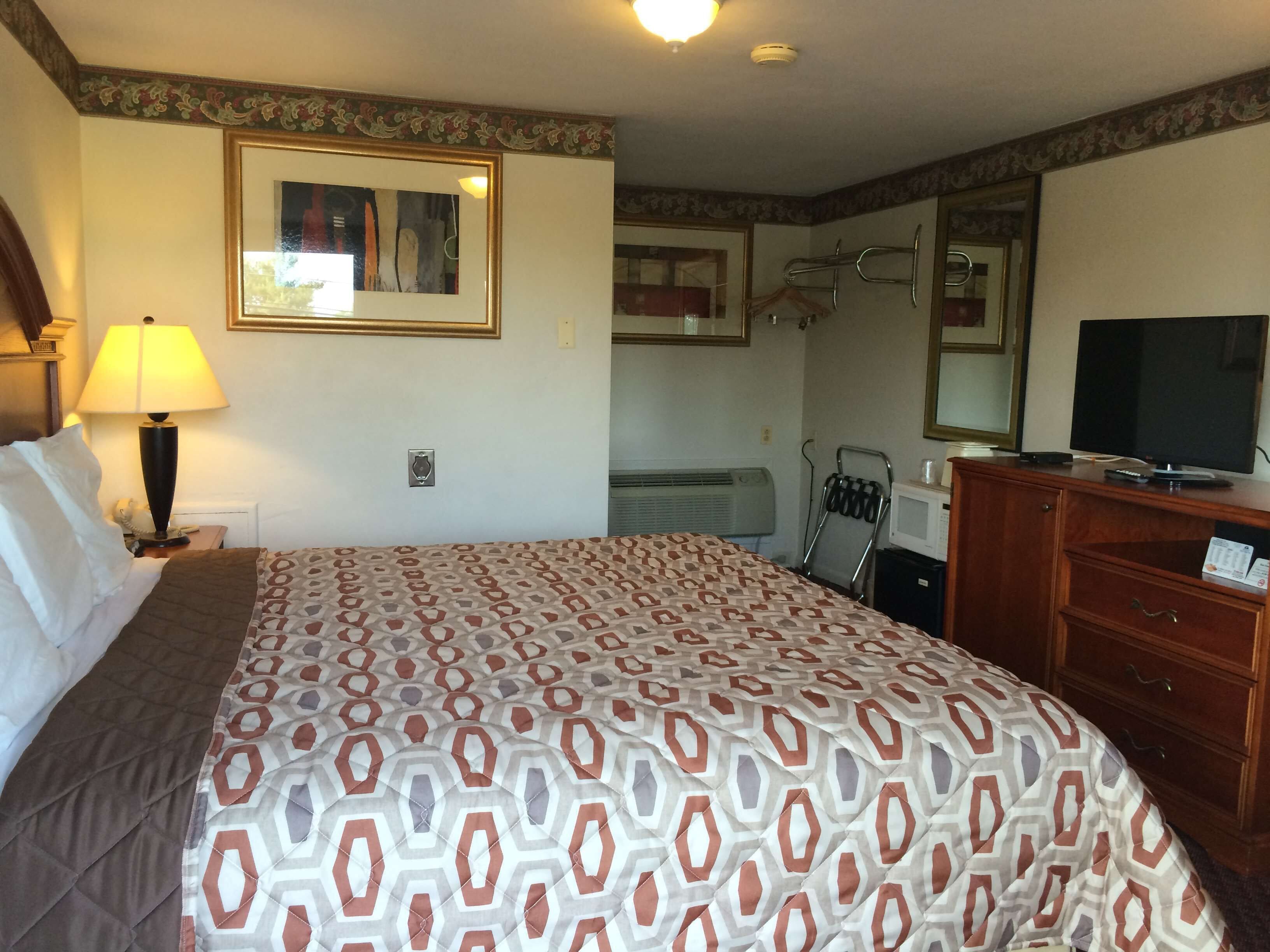 A hotel room with a bed, a lamp, a television, a dresser, and a mirror.