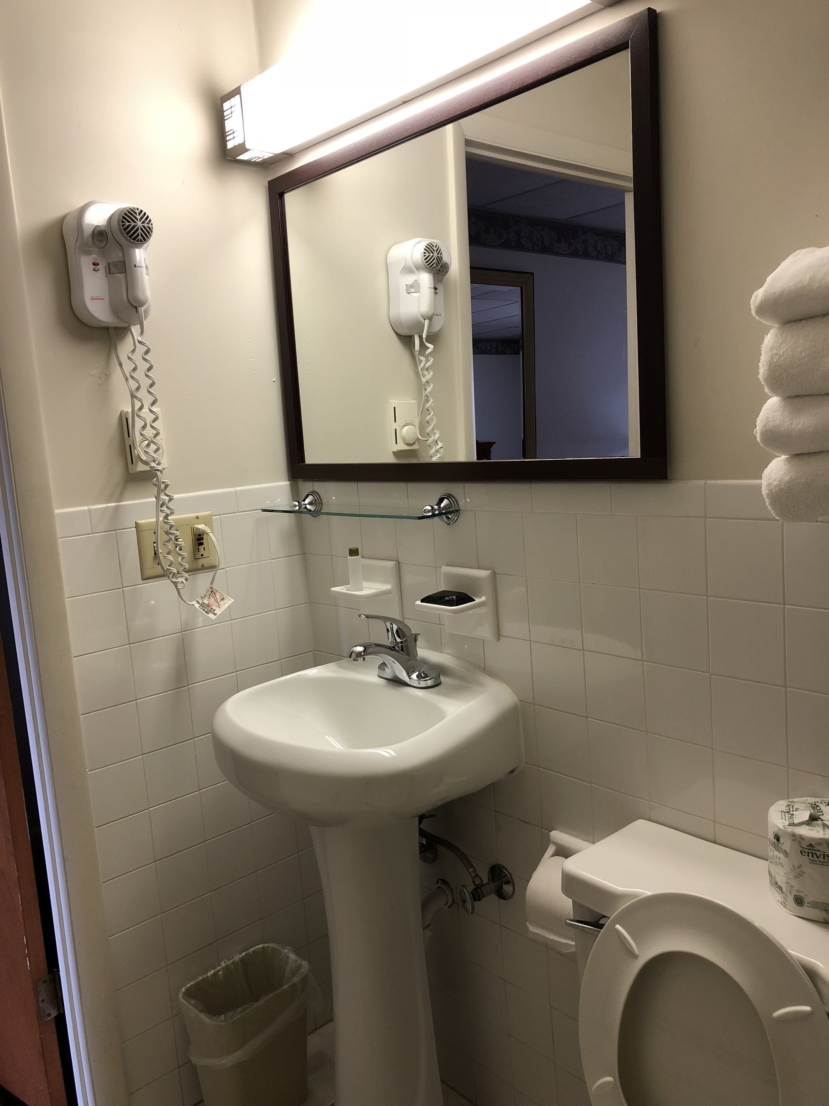 Un baño con lavamanos blanco, espejo, secador de pelo y retrete.
