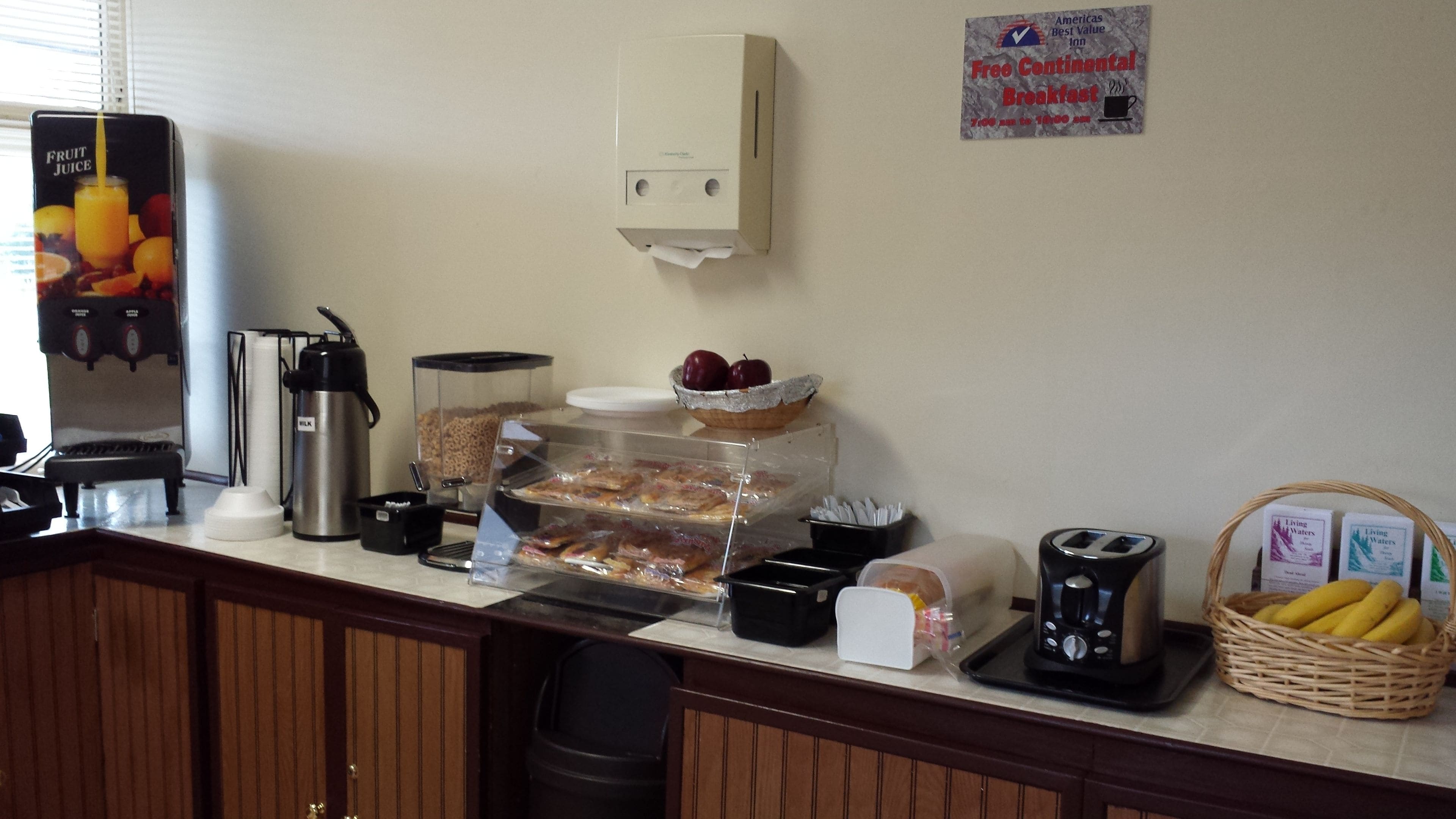 A breakfast bar with a fruit juice dispenser, a coffee maker, and a sign offering free continental breakfast.