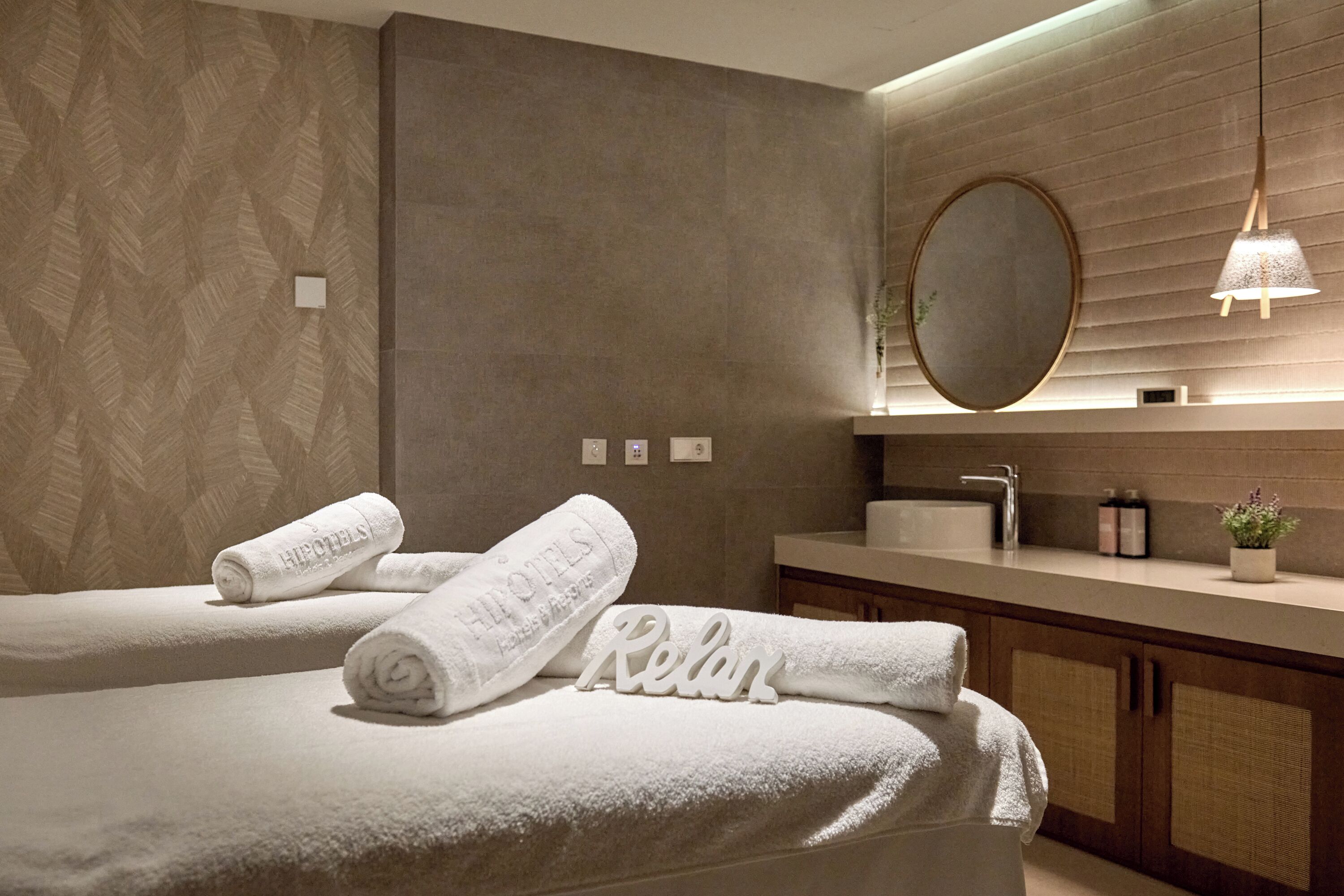 Ein modernes Hotelzimmer mit zwei Betten, einem großen Spiegel, einem Waschbecken und einer kleinen Pflanze auf der Ablagefläche.