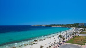 Una playa con cielo azul despejado, orilla arenosa y una hilera de edificios al fondo.