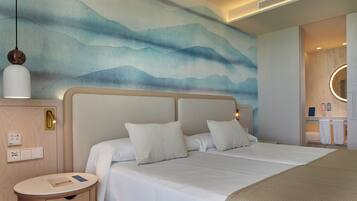 Hotellihuone, jossa on suuri sänky, yöpöytä, seinään kiinnitetty valaisin sekä kylpyhuone, jossa on peili ja pyyheteline.