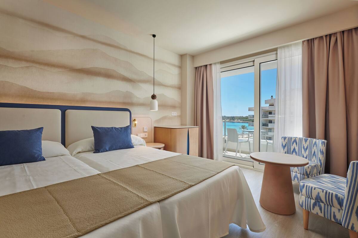 A hotel room with two beds, a round table, and a chair.