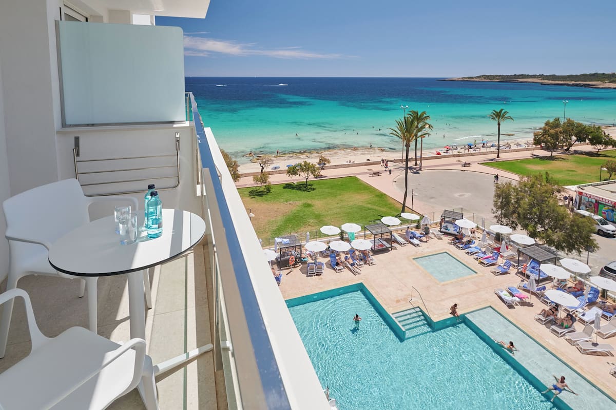 A balcony with a pool, lounge chairs, and a view of the beach and ocean.