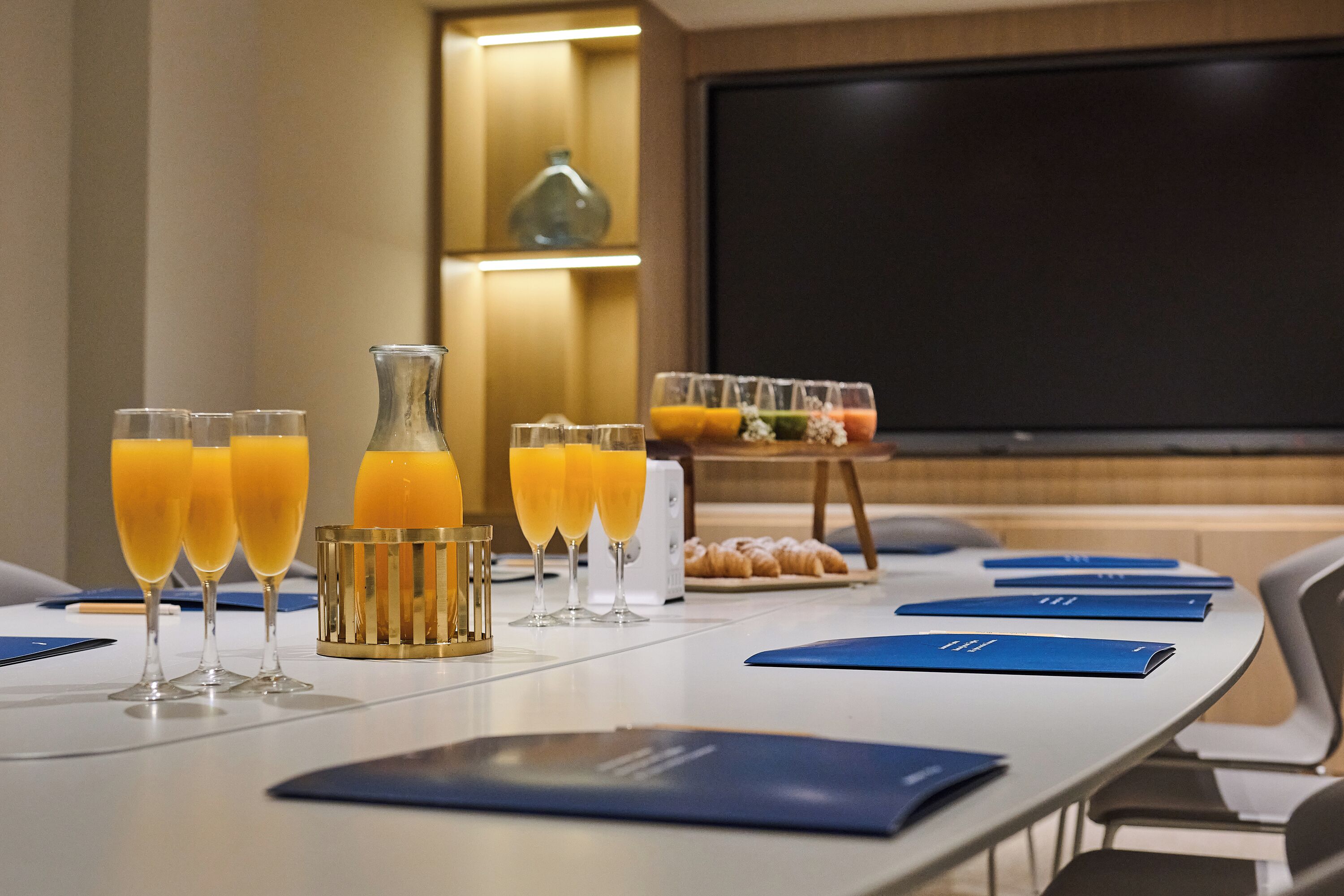 Una mesa de conferencias con varios vasos de zumo de naranja, una botella y carpetas azules.