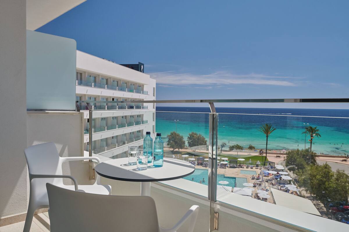 A balcony with a glass railing overlooking a pool and beach.