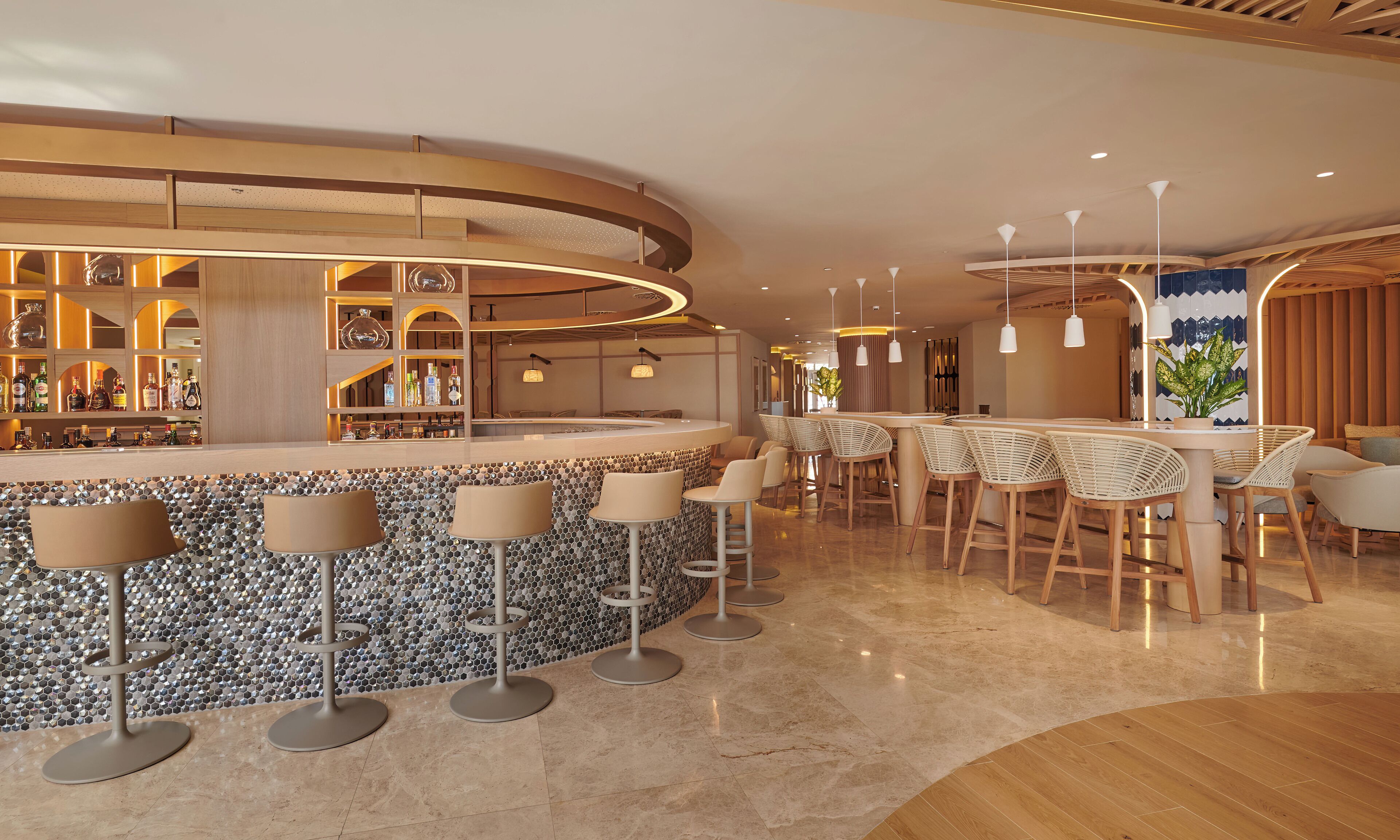 A modern bar area with a circular counter, bar stools, and a variety of bottles.