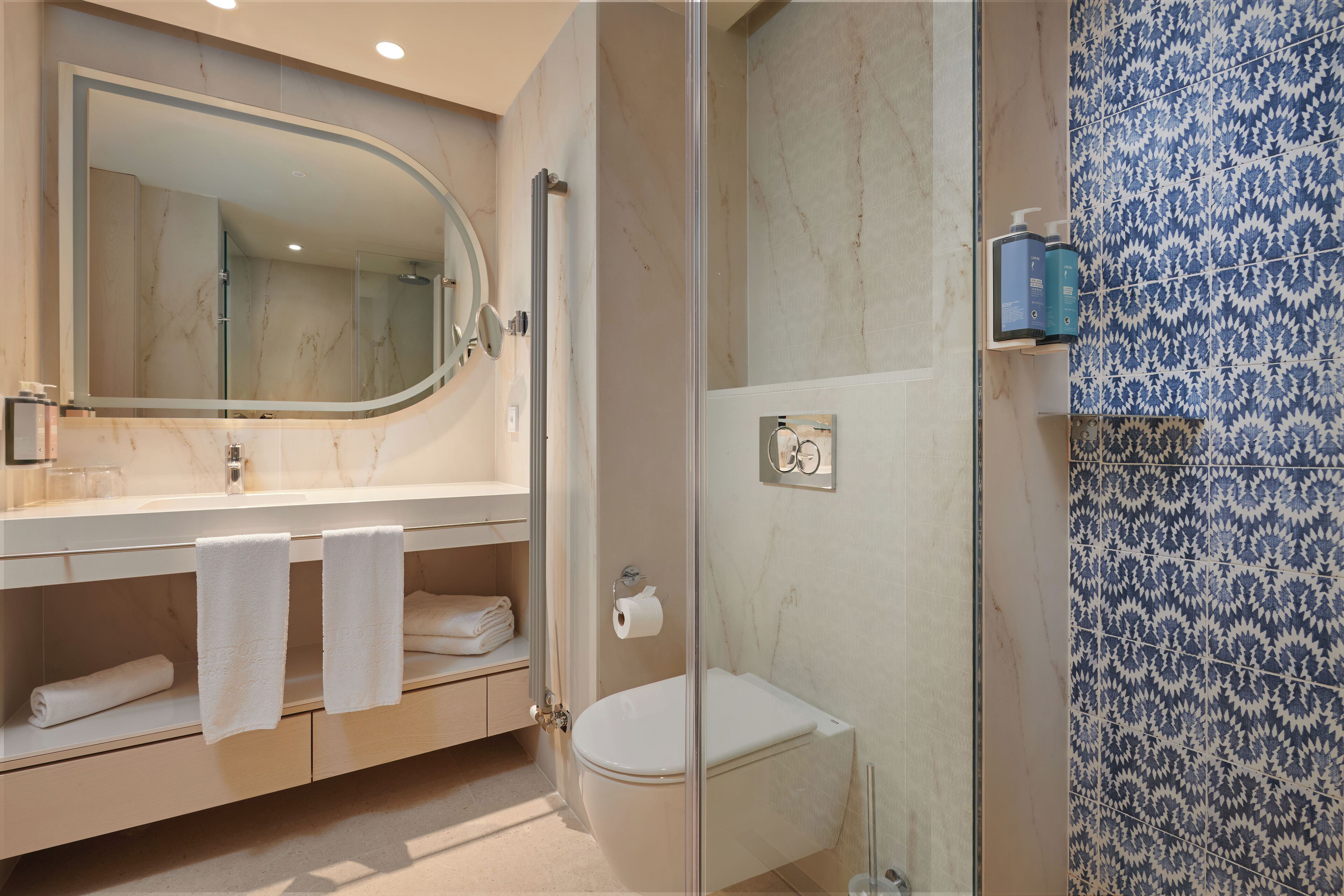 A modern bathroom with a glass-enclosed shower, a white toilet, and a vanity with a large mirror and towel racks.
