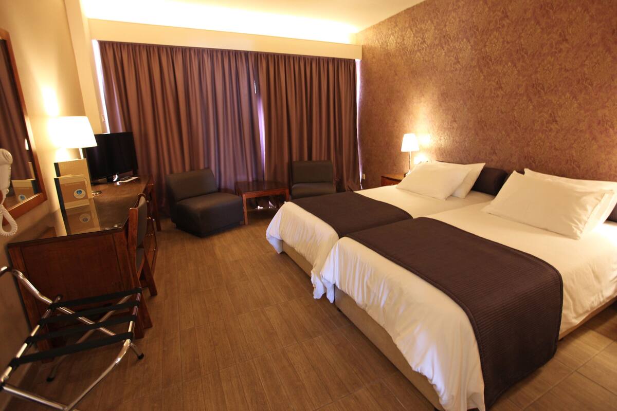 Ein Hotelzimmer mit einem großen Bett, zwei Nachttischen, einem Schreibtisch mit Stuhl, einem Fön und einem Spiegel.