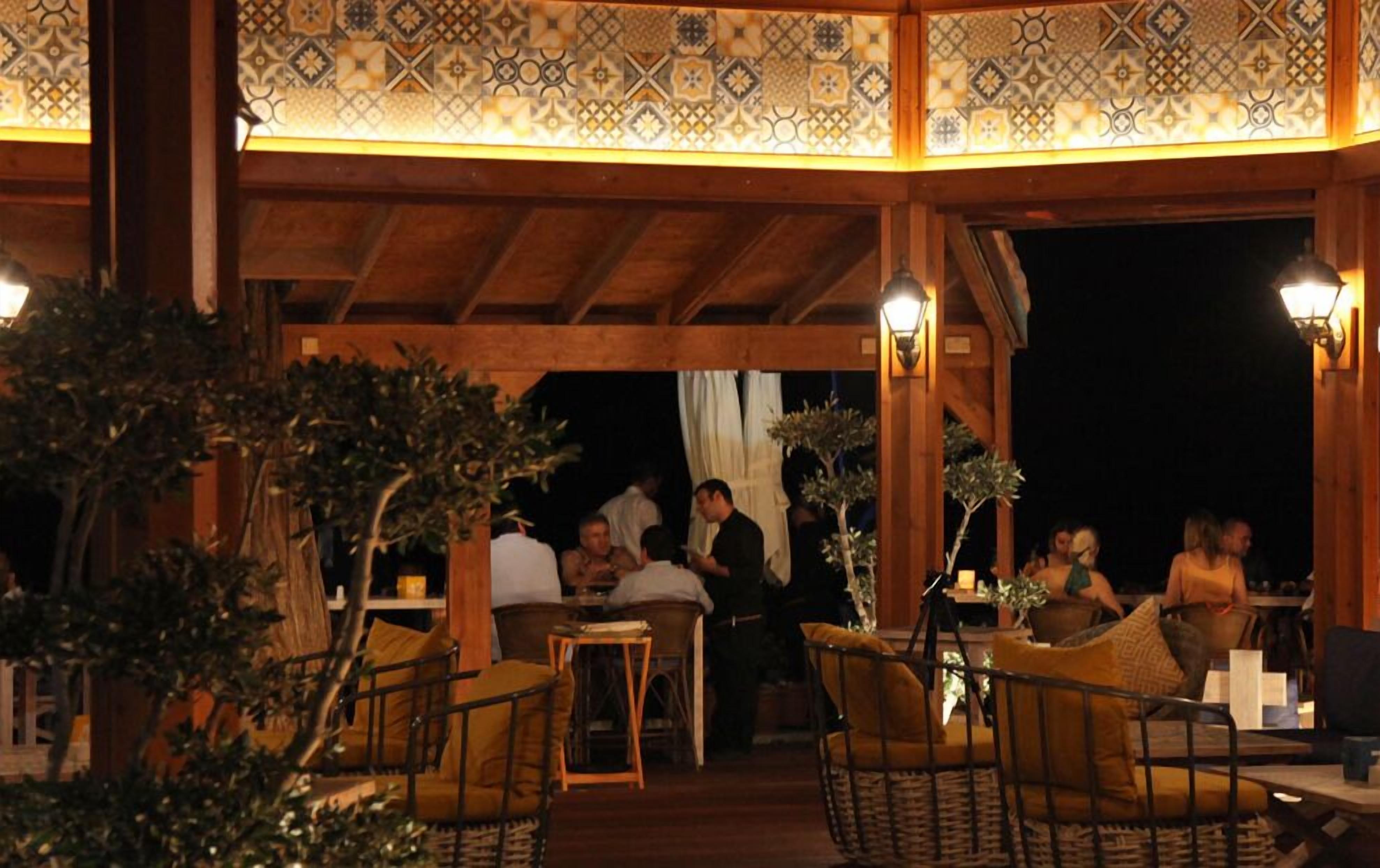 Un área de patio al aire libre con muebles y mesas de madera, rodeada de azulejos decorativos y plantas.