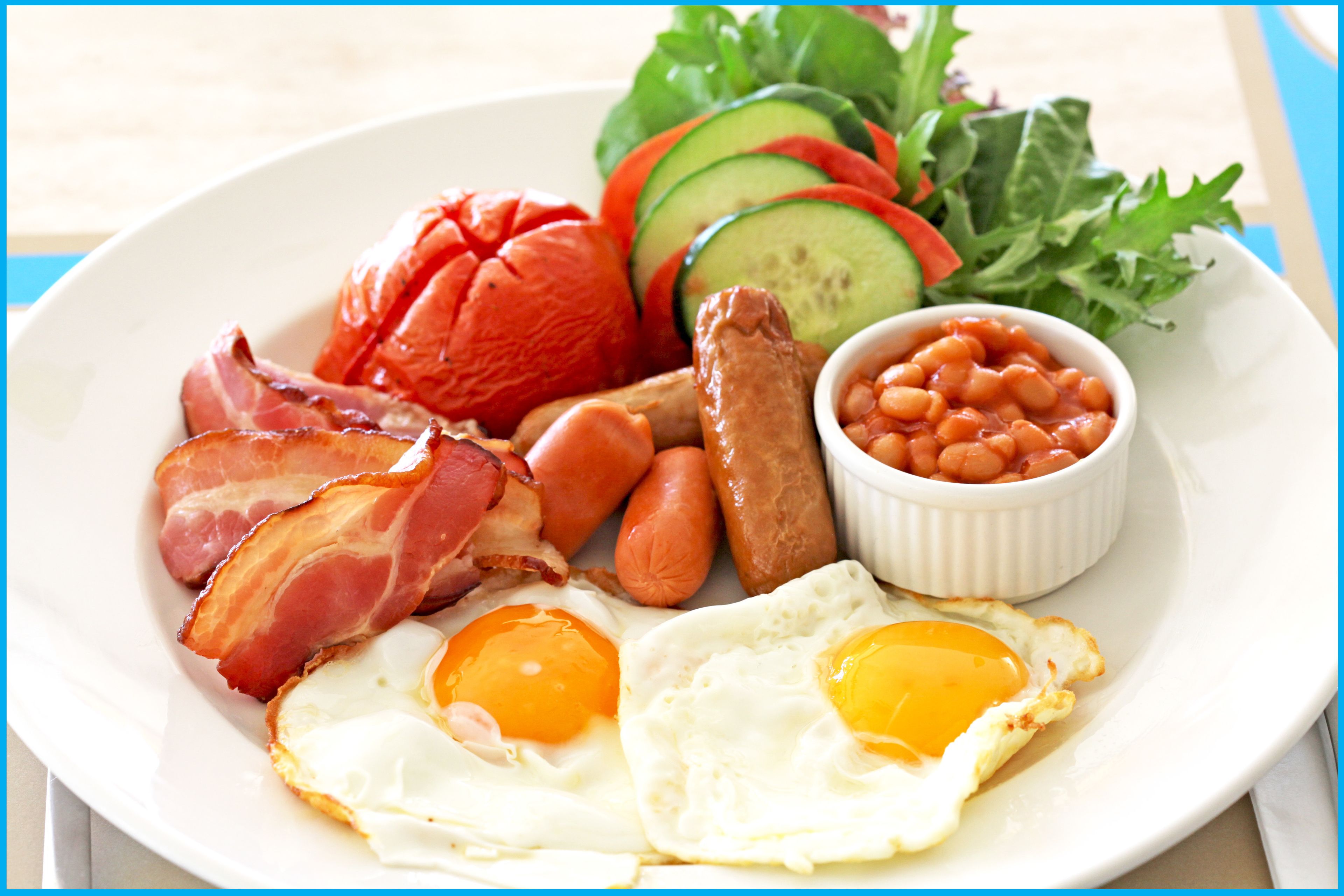 Un plato con tocino, salchichas, huevos, frijoles y verduras en rodajas.