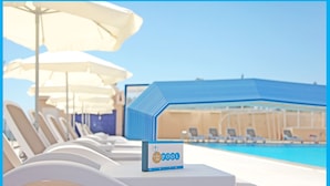 Zona junto a la piscina con sillones y sombrillas, un cartel que indica el Bar Trident, y un edificio azul al fondo.