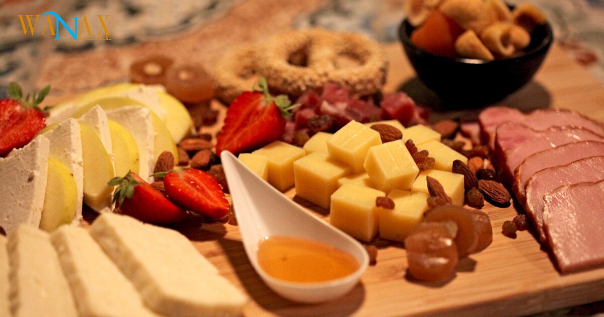 A variety of cheeses, fruits, and nuts on a wooden board.