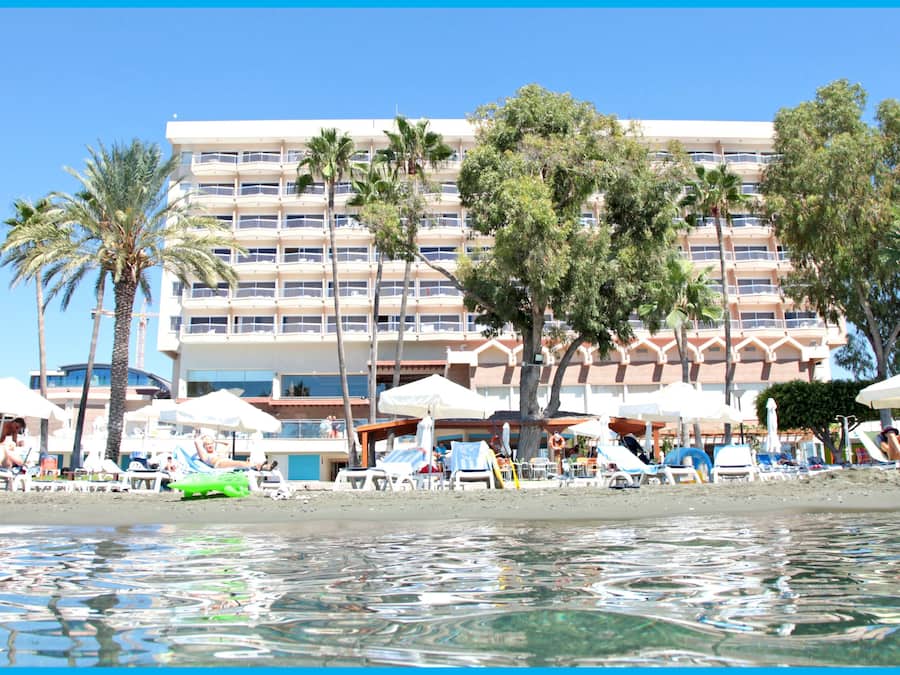 Hotel à beira-mar com várias varandas, palmeiras e guarda-sóis de praia.