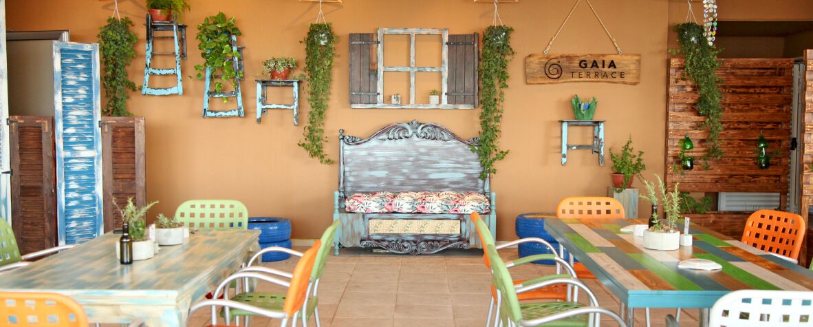 A cozy outdoor seating area with a wooden bench, colorful chairs, and tables.